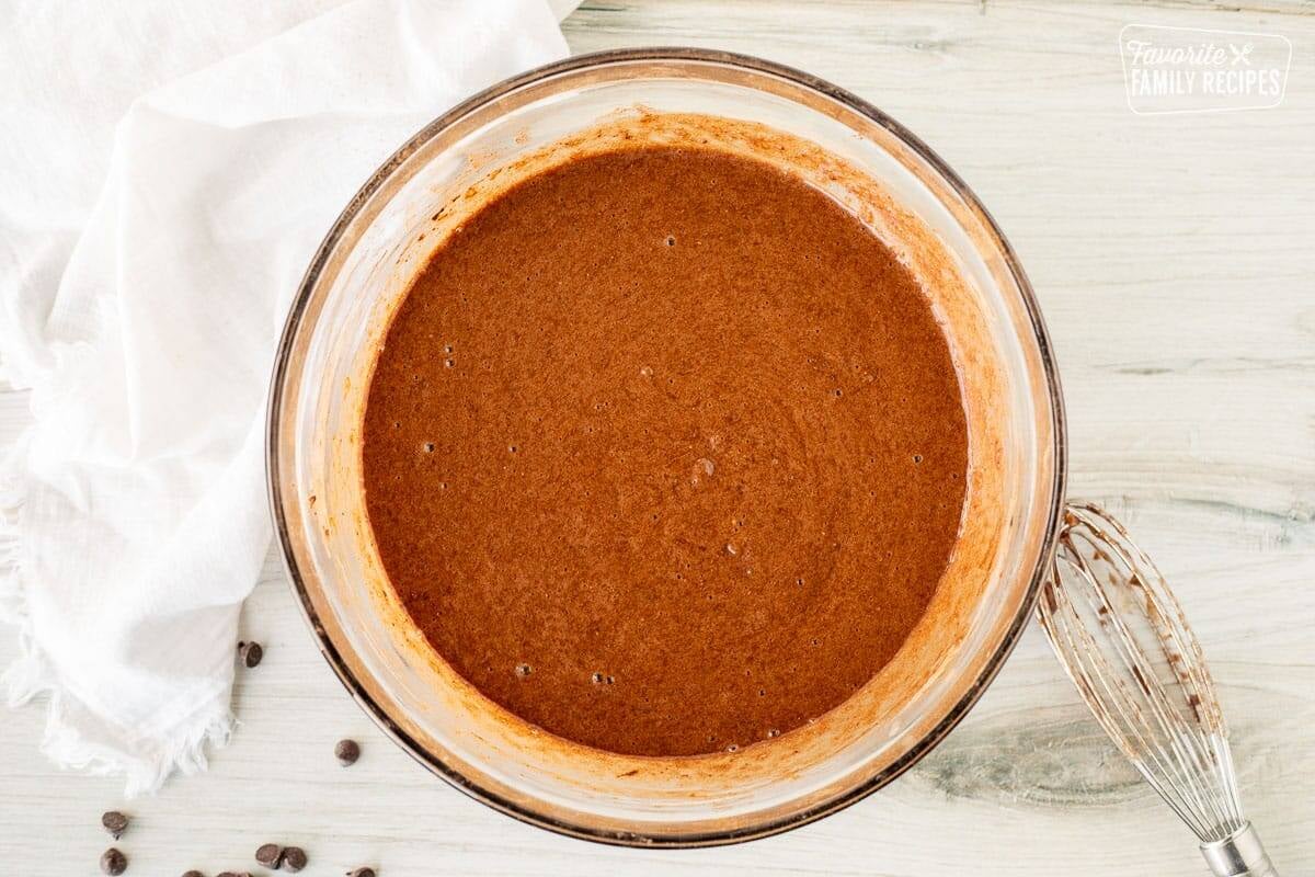 Glass bowl with chocolate muffin batter base. Whisk on the side.