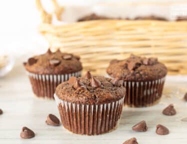 Three Healthy Chocolate Chip muffins in front of a basket of muffins.