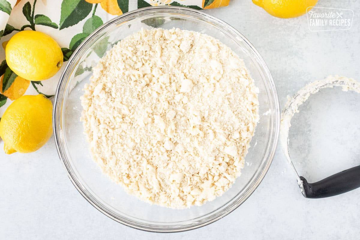 Glass mixing bowl of combined crust ingredients. Pastry blender on the side.