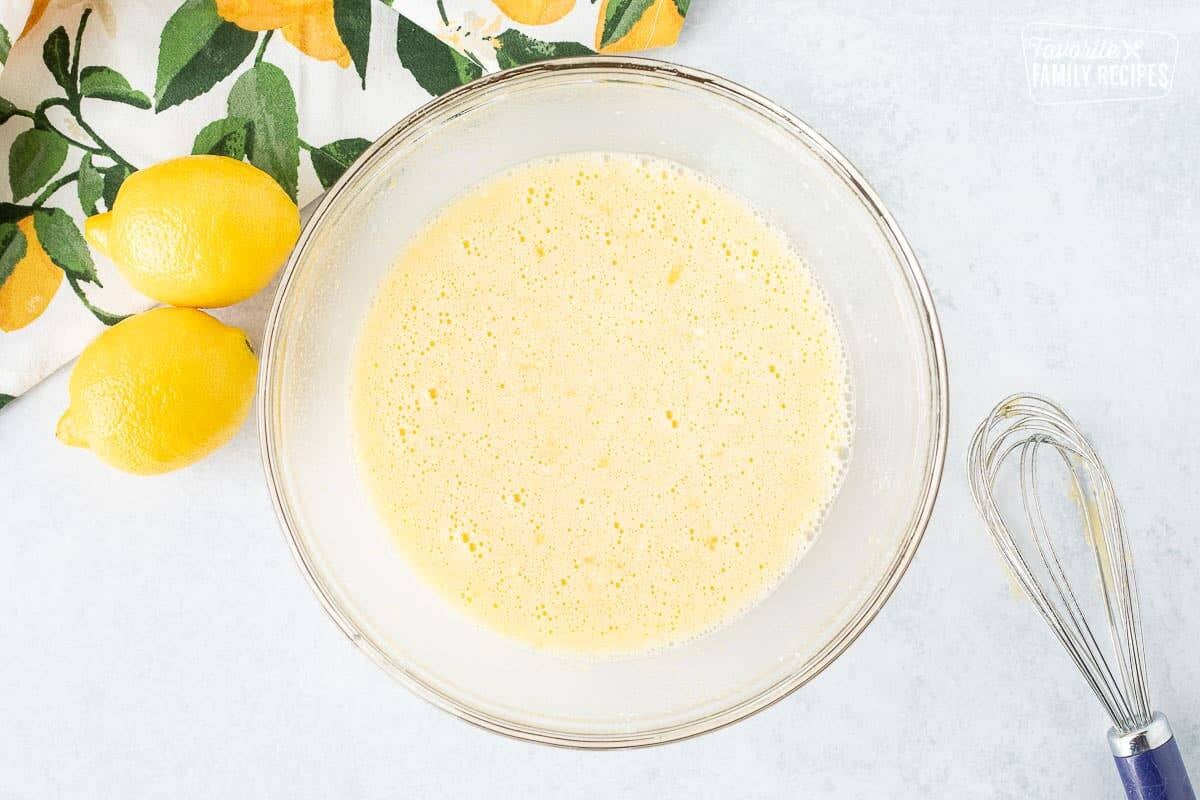 Glass mixing bowl of combined lemon ingredients. Whisk on the side.