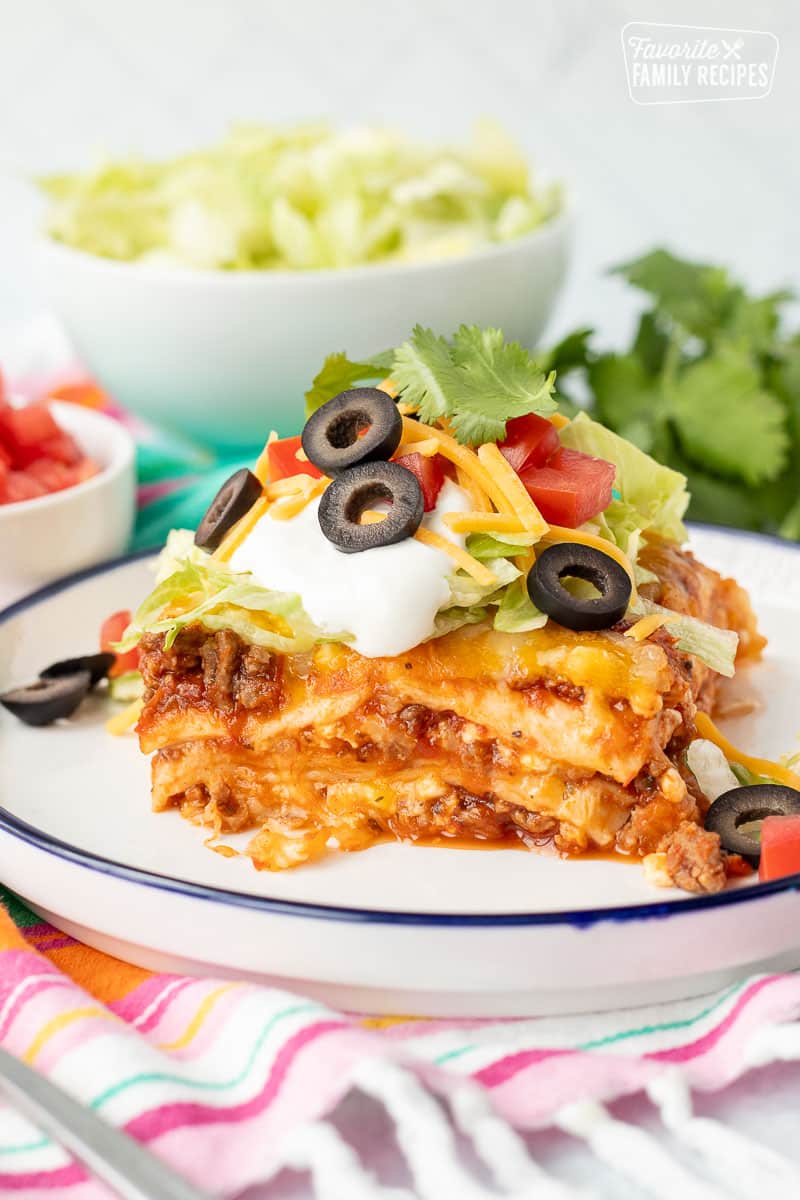 Glass plate with a slice of Mexican Lasagna with sour cream, lettuce, olives, cheese and cilantro.