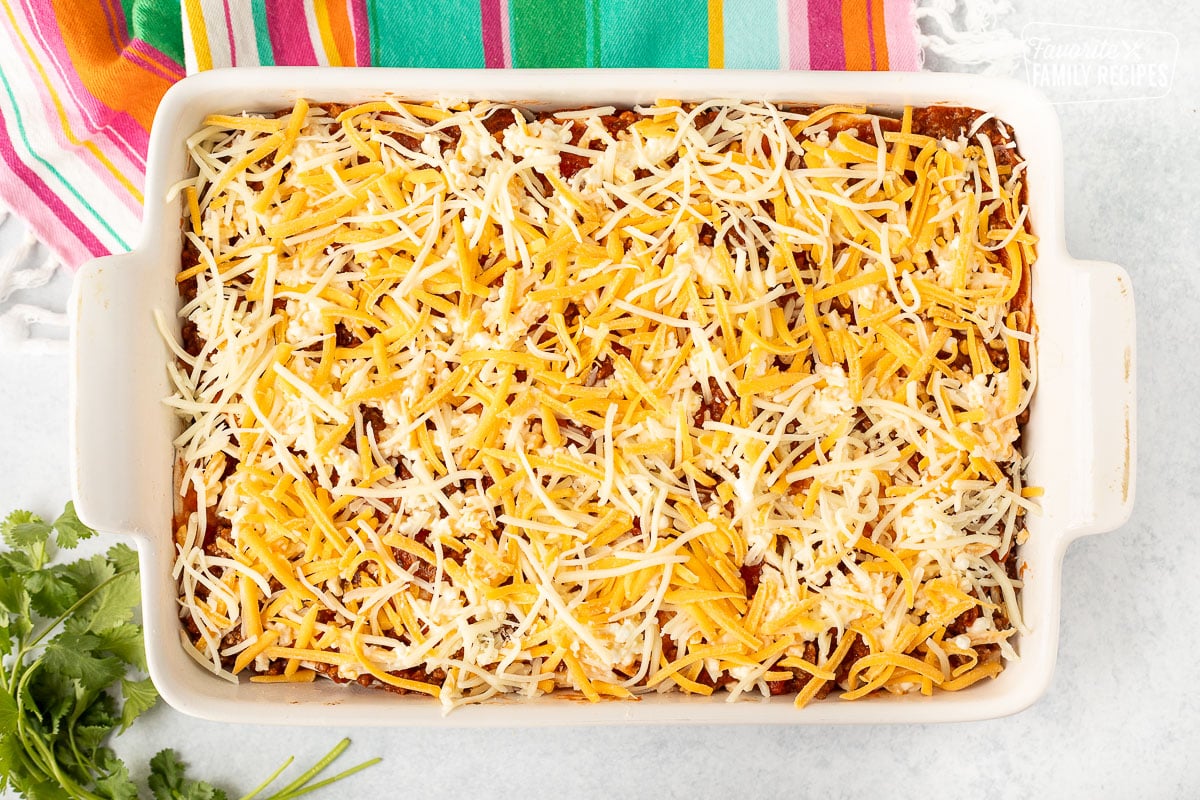 Glass baking dish with shredded cheese on top of Mexican Lasagna.