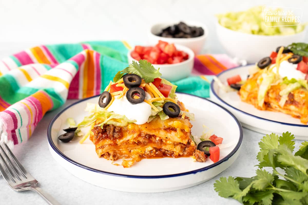 Plated Mexican Lasagna topped with shredded lettuce, cheese, sour cream, black olives, tomatoes and cilantro.