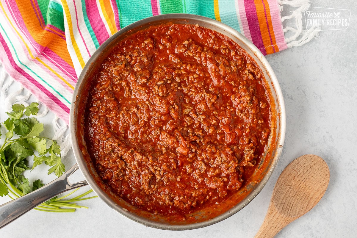 Skillet of marinara sauce and ground beef. Wooden spoon on the side.