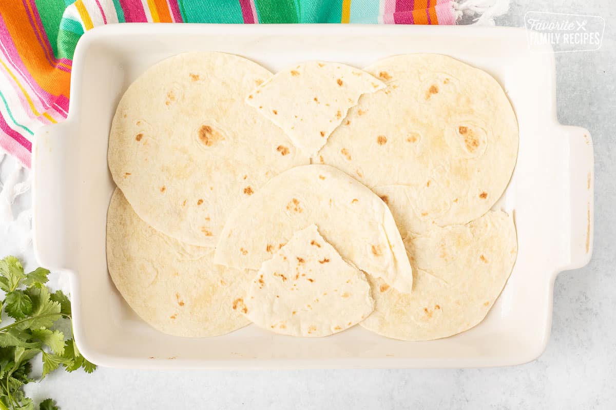 Tortillas placed on the bottom of a glass baking dish.