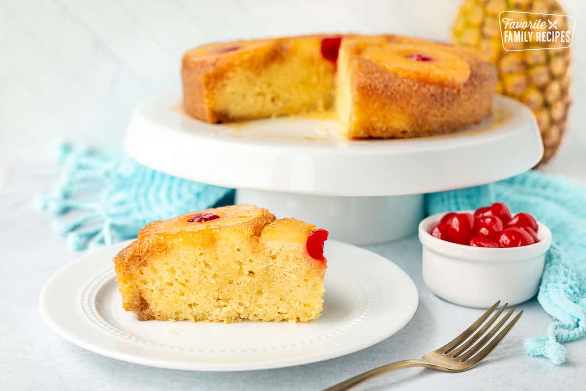 Slice of Pineapple Upside Down Cake on a plate next to cake stand with Pineapple Upside Down Cake.