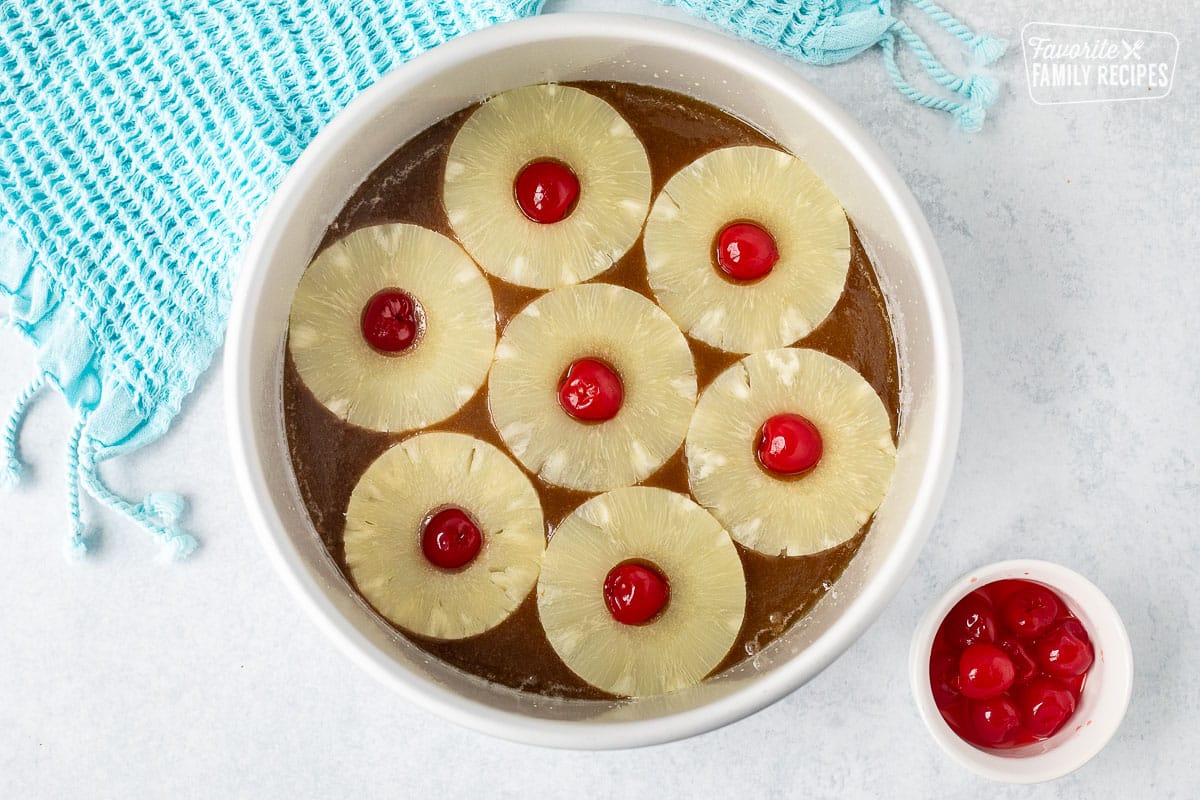 Cake round pan with caramel topping topped with pineapple slices and maraschino cherries.
