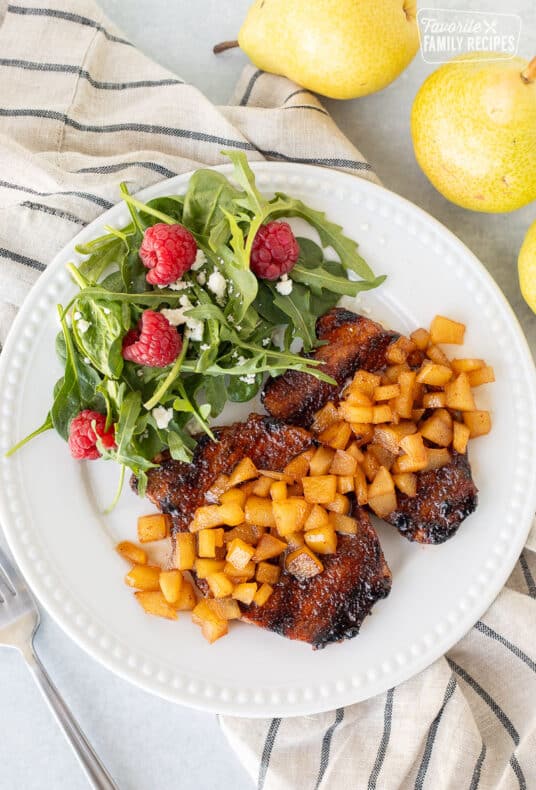 Two Grilled Pork Chops with Spiced Pears on a plate with a green salad.