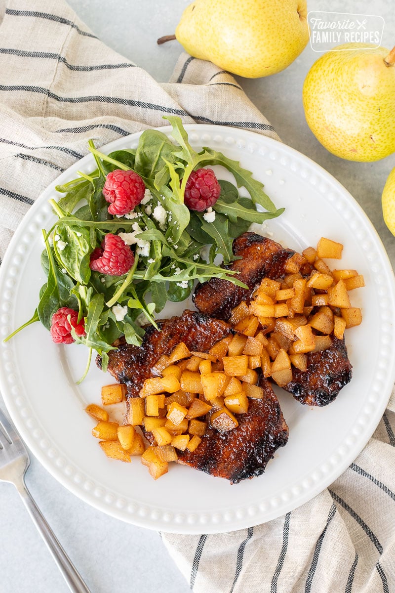 Two Grilled Pork Chops with Spiced Pears on a plate with a green salad.