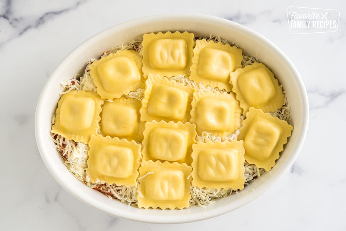 A casserole dish with layers of meat sauce, cheese mixture, and ravioli