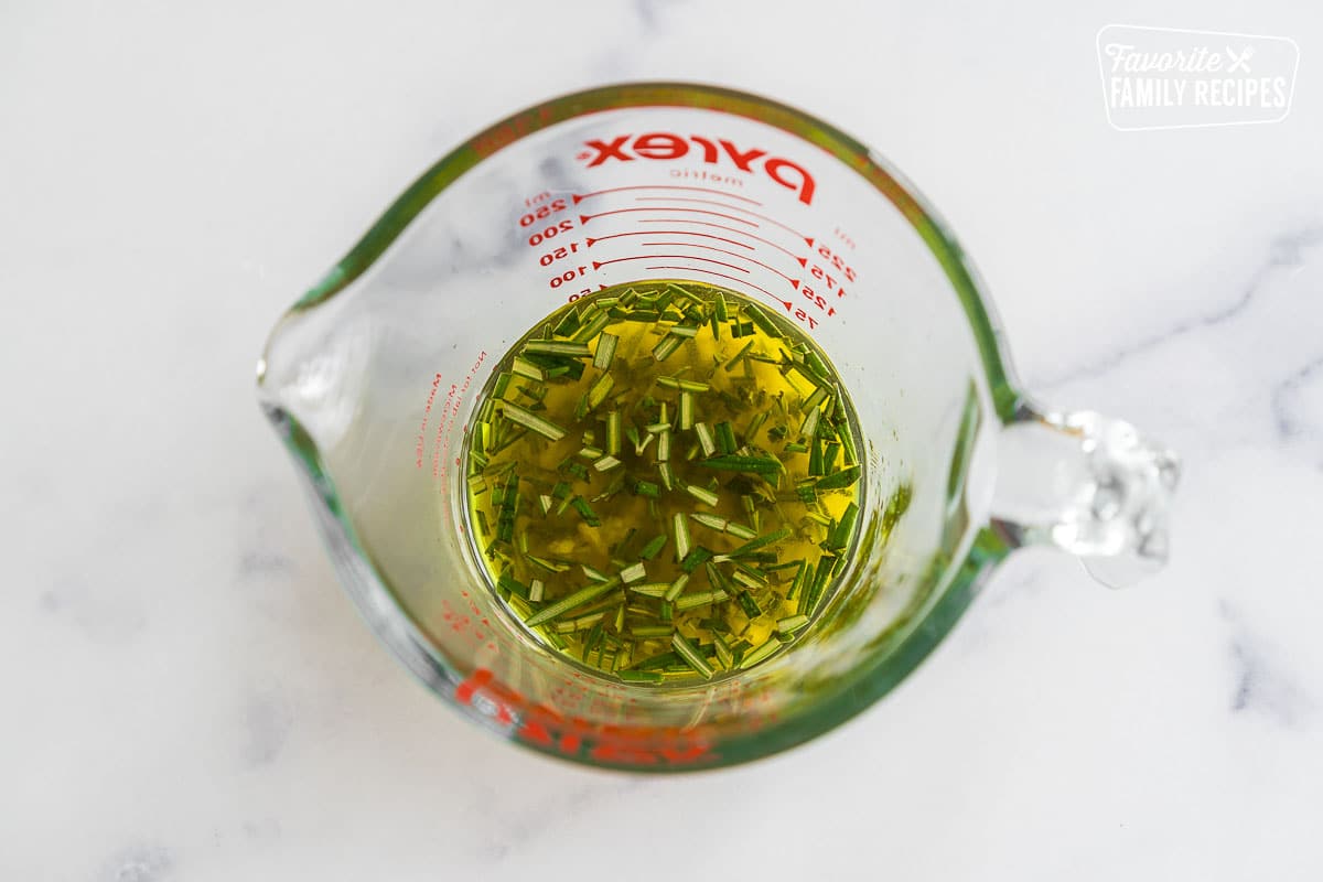 herb infused olive oil in a glass measuring cup