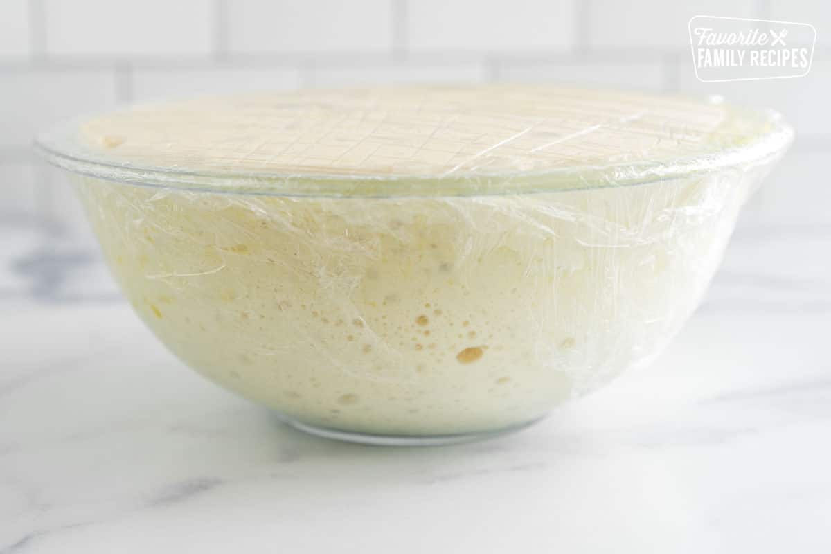 risen, bubbly dough in a large glass bowl covered with plastic wrap