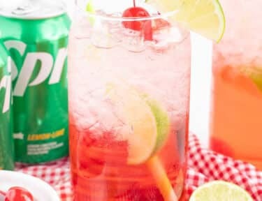 Glass of Cherry Limeade with limes and cherries.
