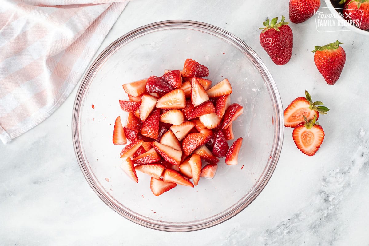 Glass bowl with sliced strawberries and sugar.