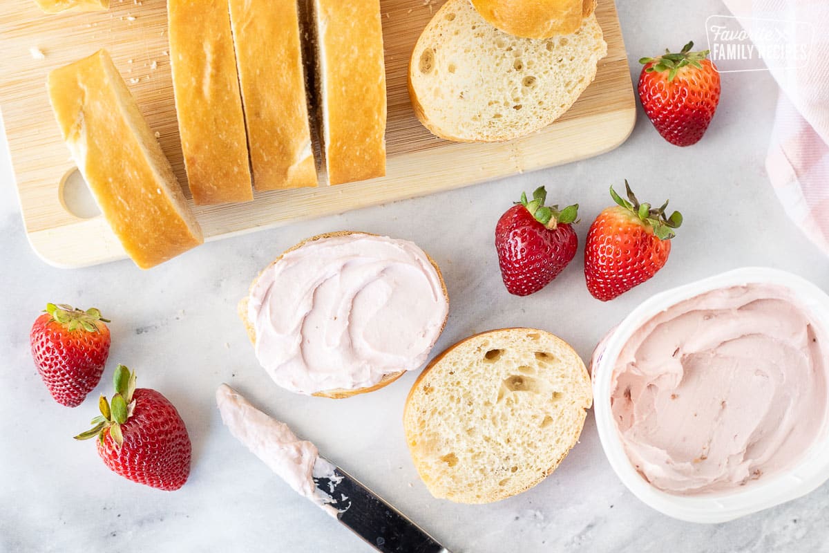 Spreading strawberry cream cheese on a slice of French bread with a knife.