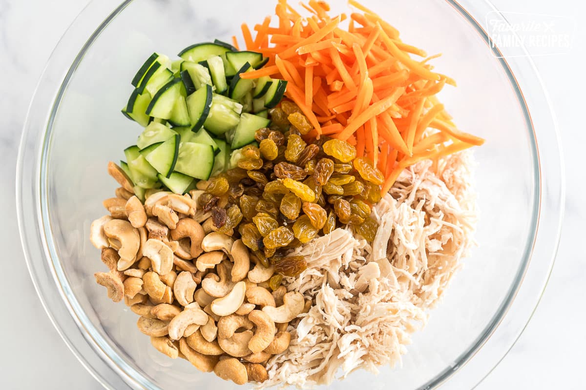 Shredded chicken, cucumbers, cashews, golden raisins, and shredded carrots in a bowl.