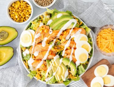 Bowl of Buffalo Chicken Salad with avocado, corn, seeds, cheese, eggs and dressing.