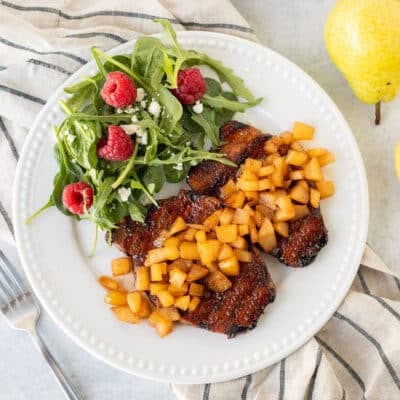 Plate with two Grilled Pork Chops with Spiced Pears next to a green salad with feta and raspberries.