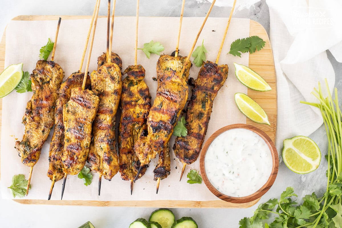 Thai chicken skewers on a cutting board with yogurt dip on the side.