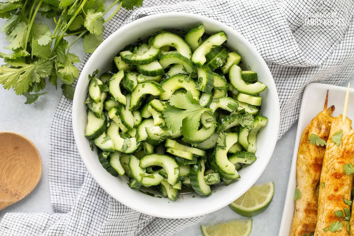 Cucumber salad in a white bowl with pineapple on the side.