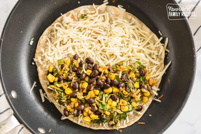 A tortilla in a skillet topped with cheese and a vegetable mixture