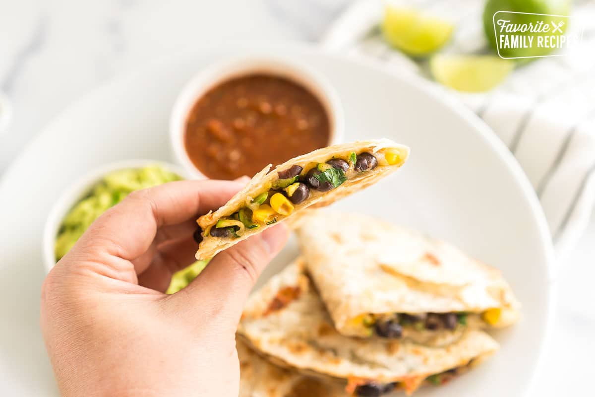A hand holding a slice of a Veggie Quesadilla.
