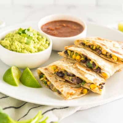 A sliced veggie quesadilla on a plate with bowls of guacamole and salsa
