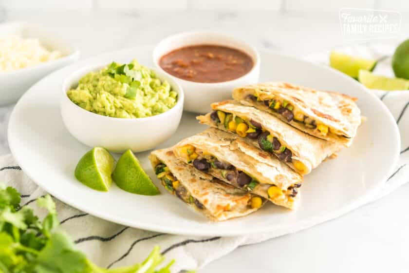 A sliced veggie quesadilla on a plate with bowls of guacamole and salsa