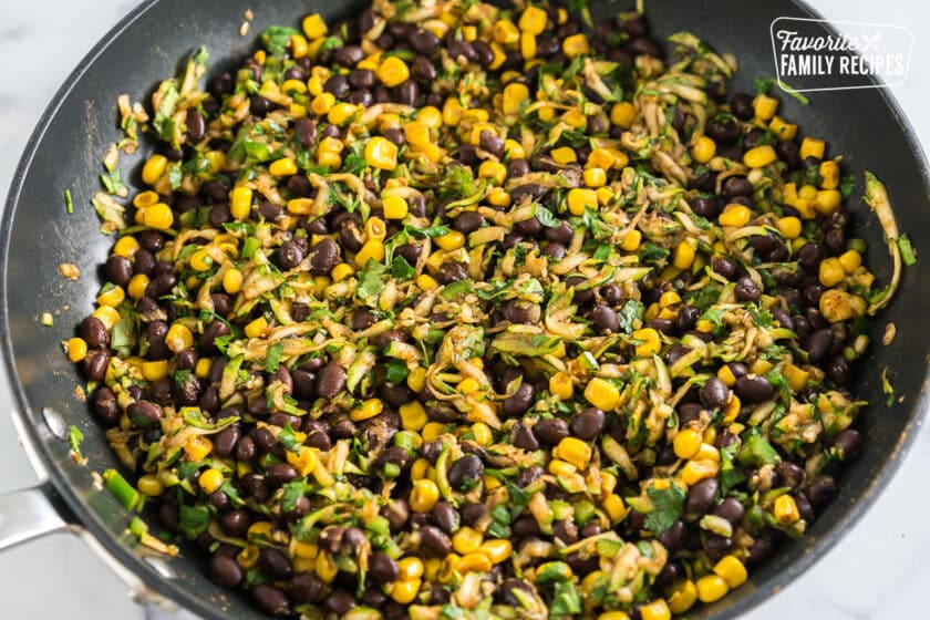 Black beans, corn, zucchini, and spices cooking in a skillet