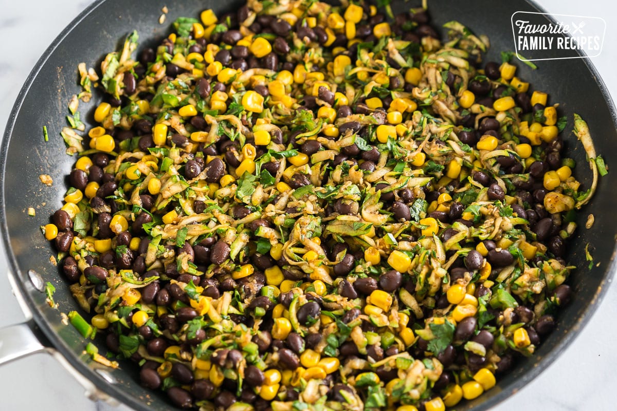 Black beans, corn, zucchini, and spices cooking in a skillet.