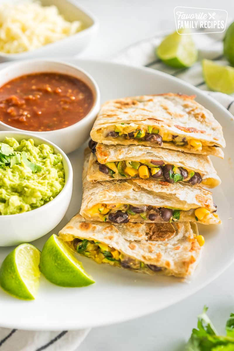 A sliced veggie quesadilla on a plate with bowls of guacamole and salsa.