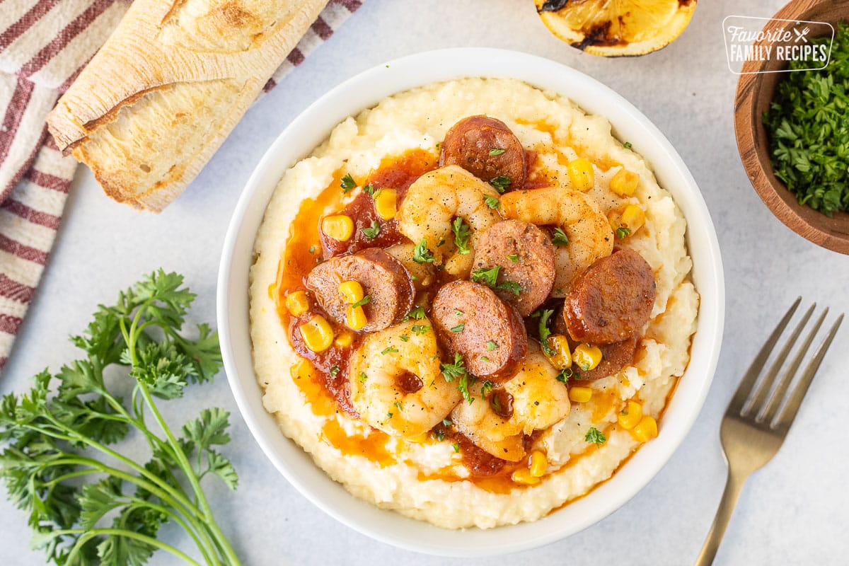 Bowl with cheesy grits, shrimp, sausage and corn garnished with parsley. Fork on the side.