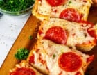 French bread pizza slices with herbs, pepperoni, and melted mozzarella, served on a wooden board with parsley and seasonings in bowls