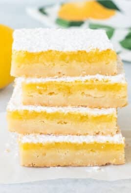 Stacked Lemon Bars next to fresh sliced lemons.