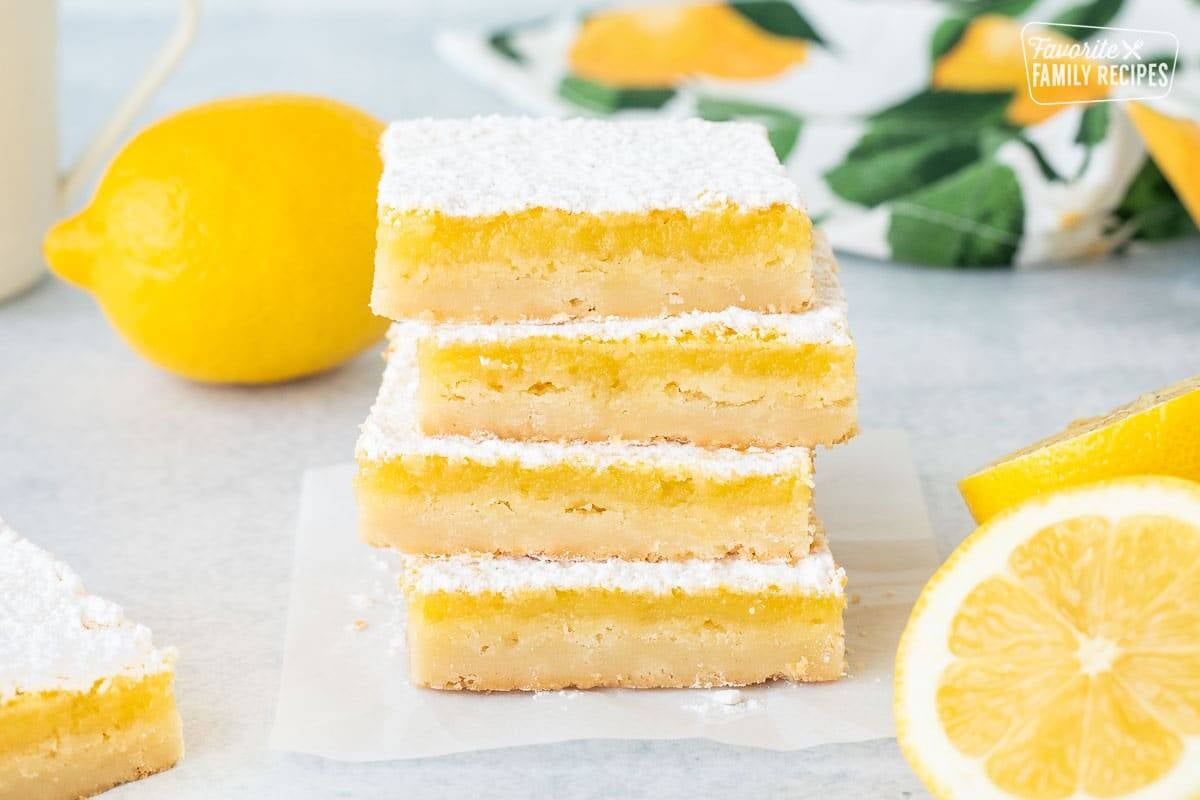 Stacked Lemon Bars next to fresh sliced lemons.