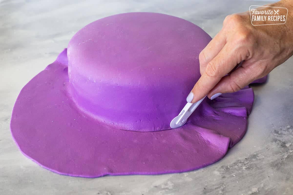 Cutting around the edge of the cake covered in purple fondant.