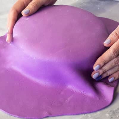 Pushing down the sides of purple fondant onto a cake.