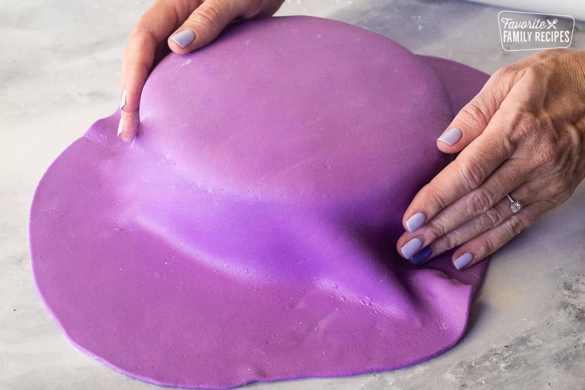 Pushing down the sides of purple fondant onto a cake.