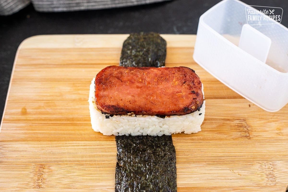 Cutting board with plastic mold on the side of unwrapped Spam Musubi.