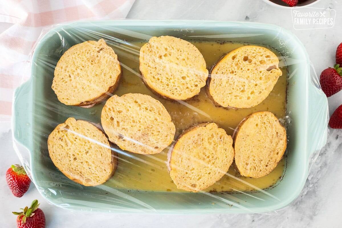 Baking dish of soaking Strawberry French Toast covered in plastic wrap.