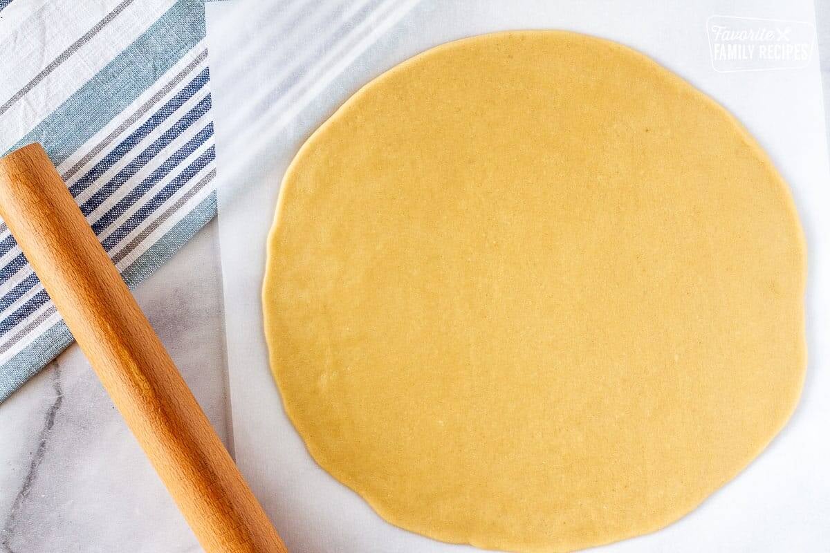 Large circular flattened cookie dough with a rolling pin on the side to make easy fruit pizza.