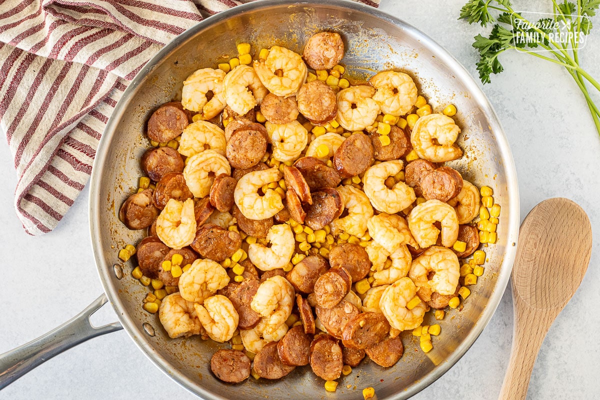Skillet with shrimp, corn and sausage. Wooden spoon on the side.