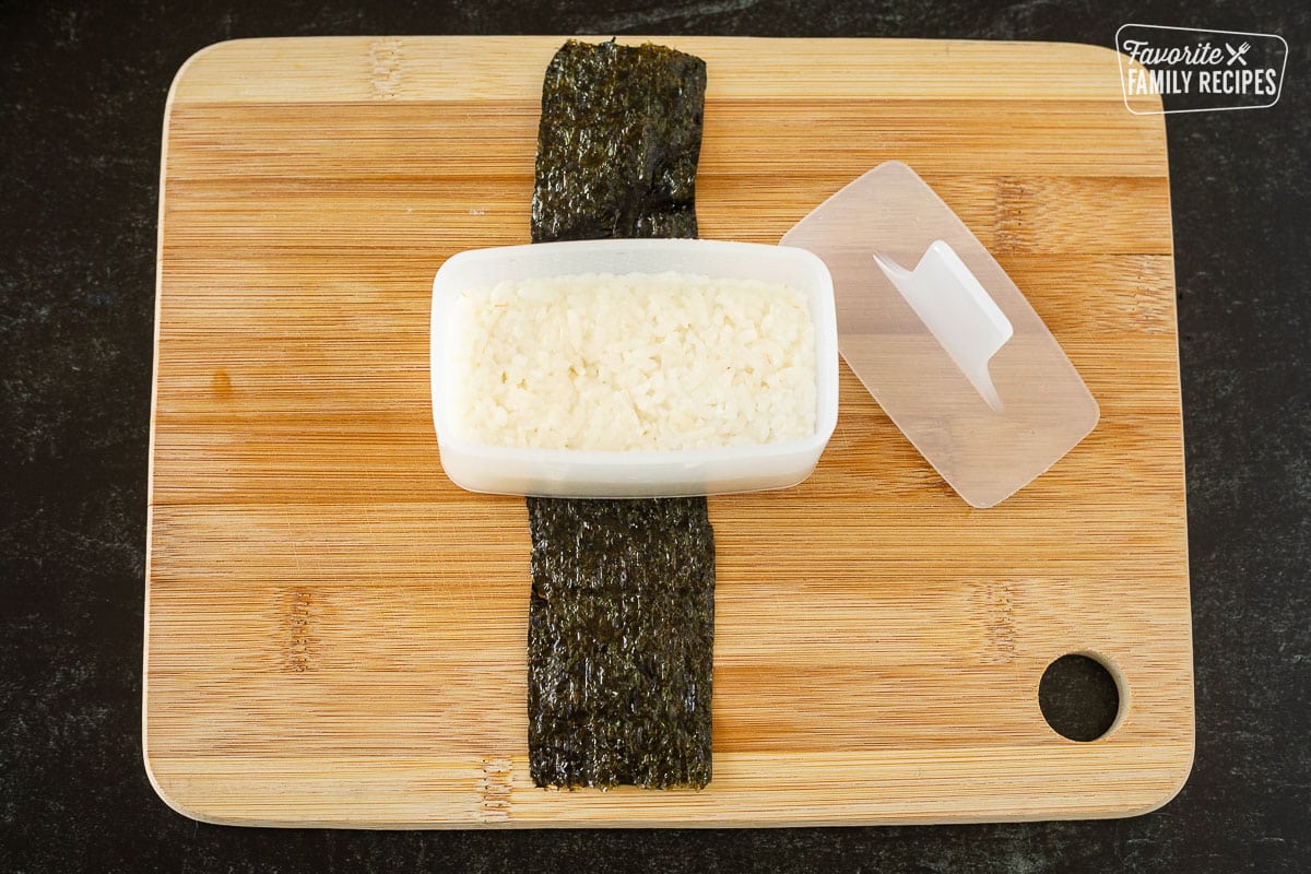 Cutting board with pressed sushi rice in musubi mold.