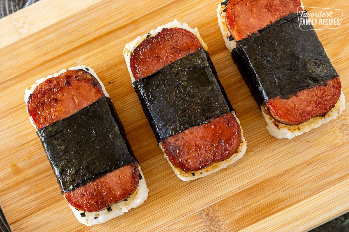 Three Spam Musubi lined up on a cutting board.