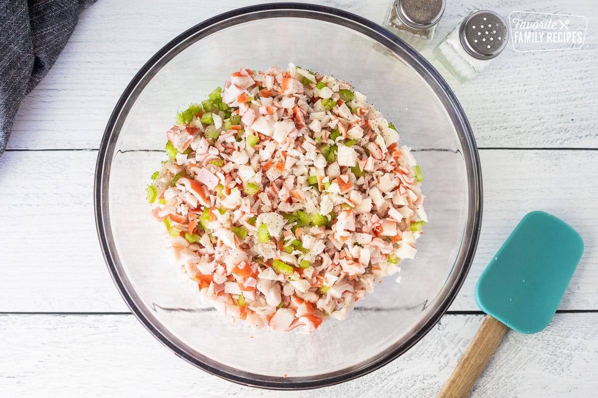 Glass mixing bowl with cut up crab and celery. Salt and pepper on the side.