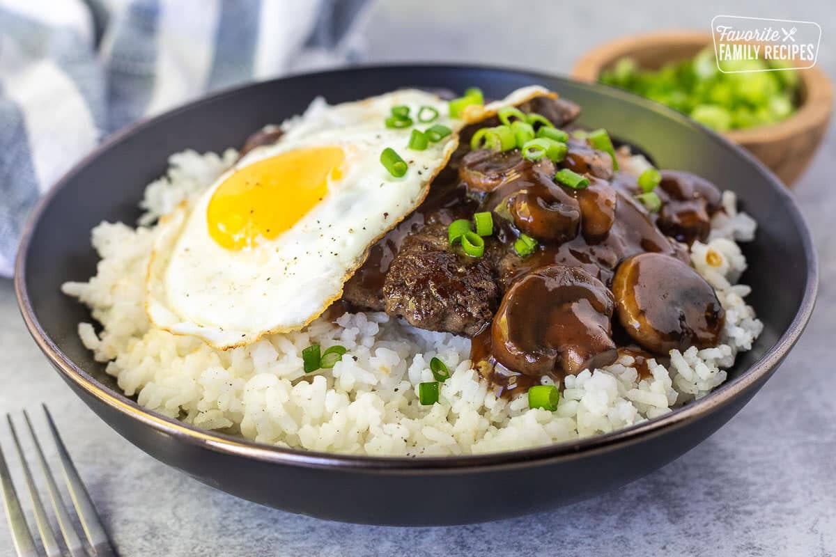 Bowl of Loco Moco with ground beef patty, egg, mushroom gravy and green onions.