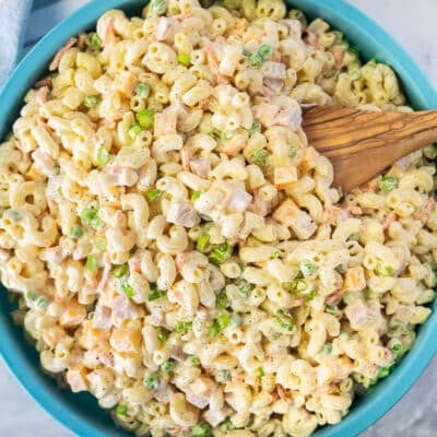 Bowl of Macaroni Salad with pasta, ham, peas, and cheese with a wooden spoon dipped in the bowl.