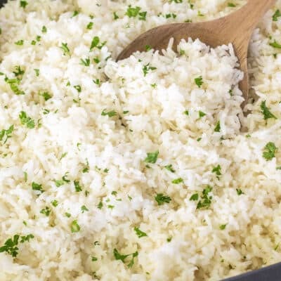 Cooked rice in a roasting pan with parsley as garnish. Wooden spoon in the pan.