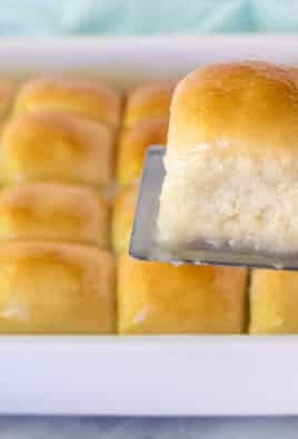 Spatula holding up a single Pani Popo roll over a pan of Samoan Coconut rolls.