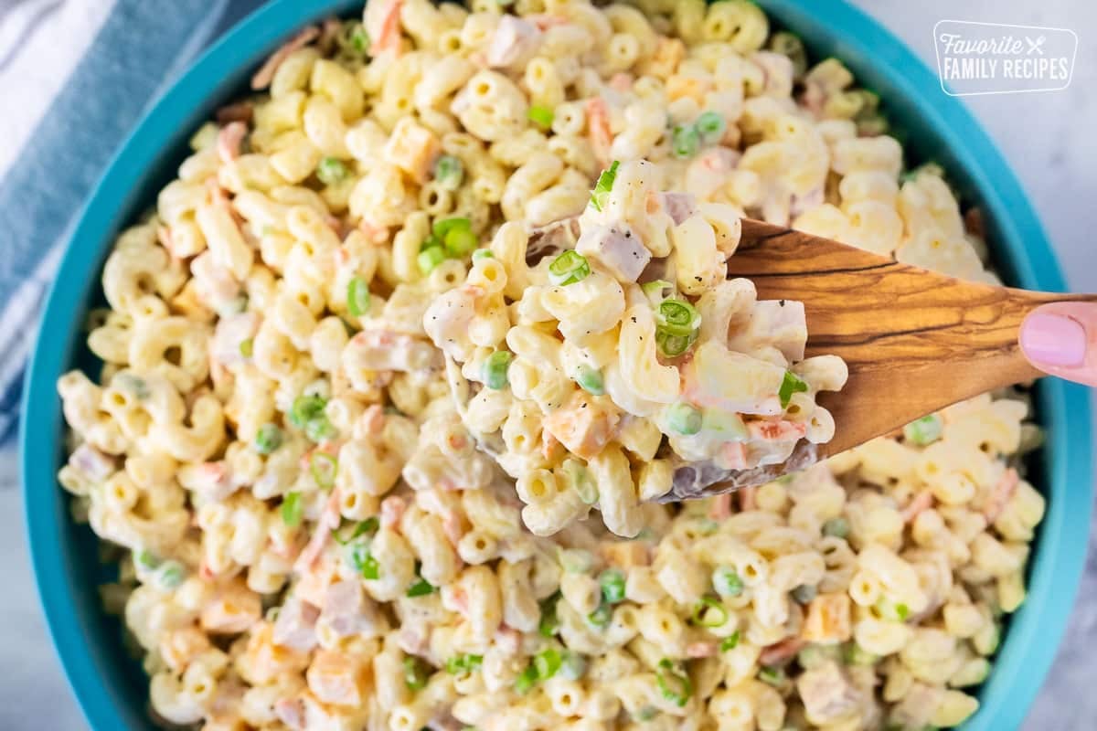 Spoon holding a scoop of Macaroni Salad from a large bowl.
